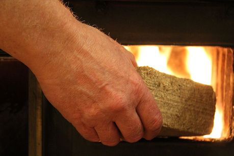 Mann legt Holzbrikett in einen Ofen